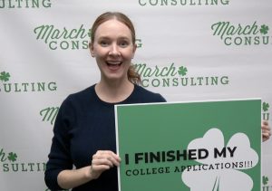 Kat Clowes of March Consulting Group is smiling big and holding a sign that says "I finished my college applications"
